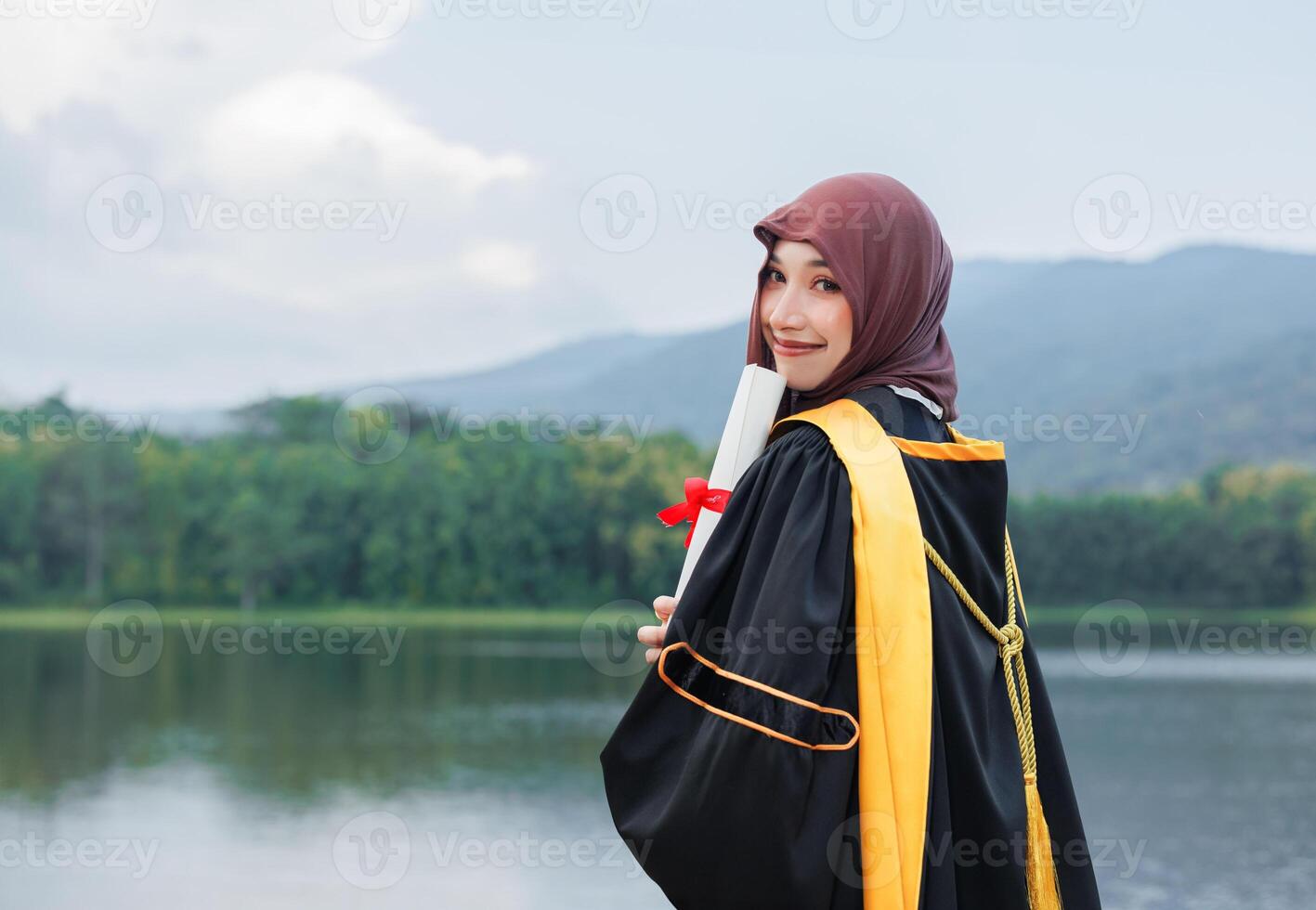 Asian muslim woman wearing hijab holding diploma and standing by lake photo