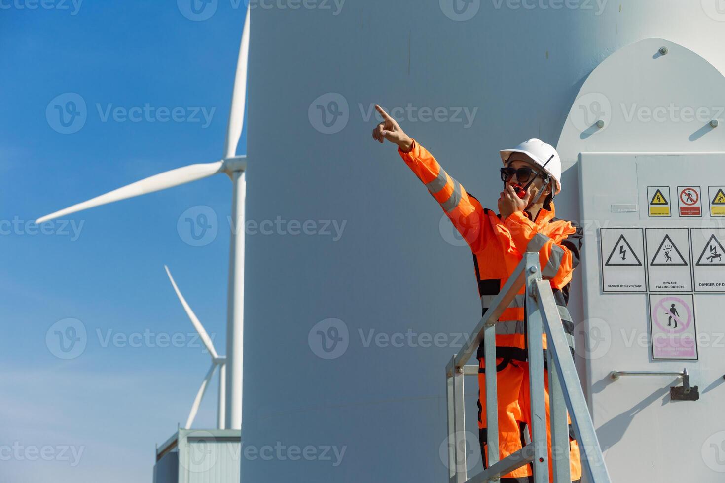 A man in an orange jacket pointing at a wind turbine photo