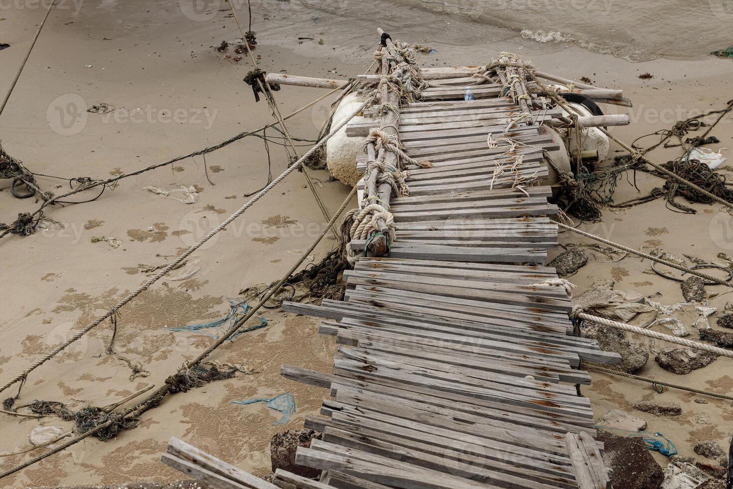 old dirt grungy decaying wooden boat bridge pier with ropes tie piled up and washed ashore on quiet sandy beach. photo