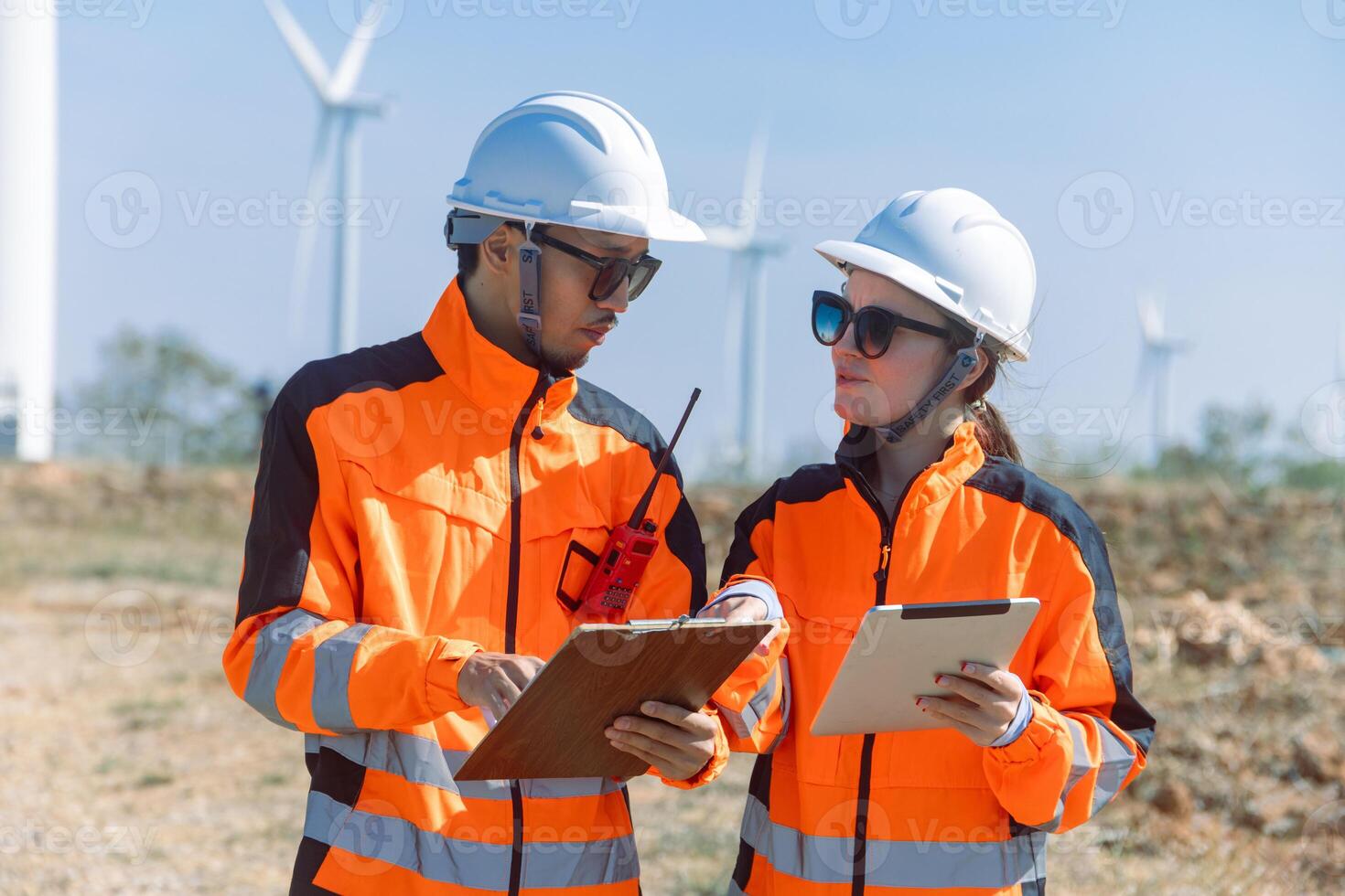 Two people in hard hats and safety vests standing next to wind turbines photo