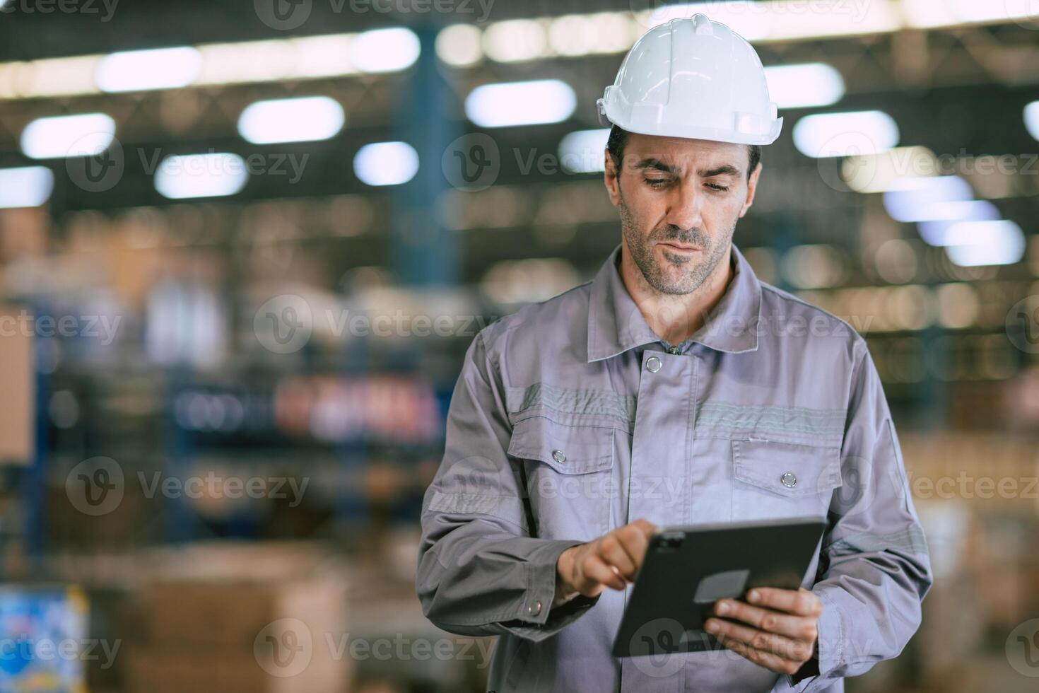 A man in a hard hat is using a tablet in a warehouse photo