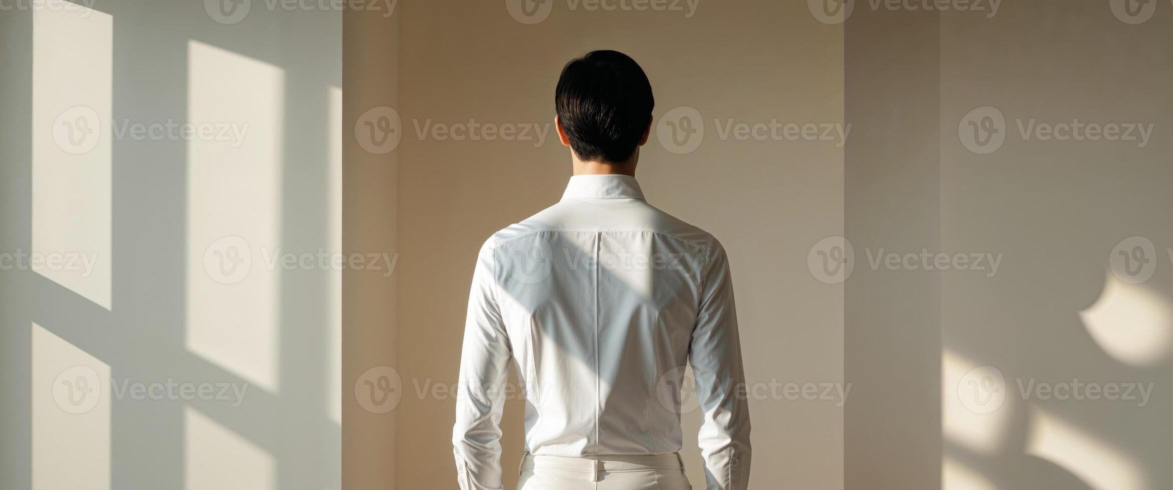Back view of person wearing white shirt with shadows on wall in soft lighting and neutral background photo