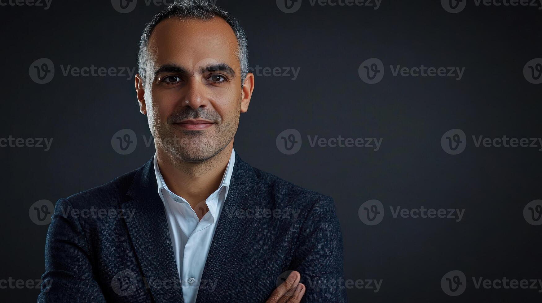 A man in a suit standing against a dark background with his arms crossed. photo