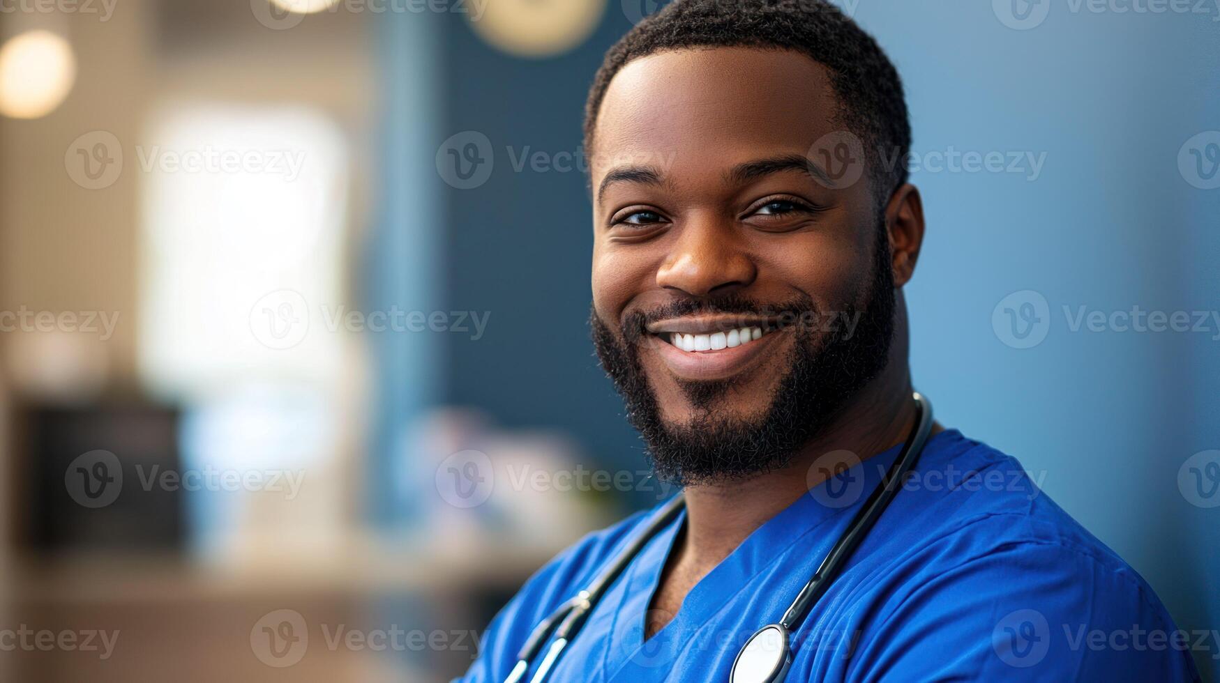 A smiling male healthcare professional in a blue uniform with a stethoscope, standing in a hospital setting with a blurred background. photo