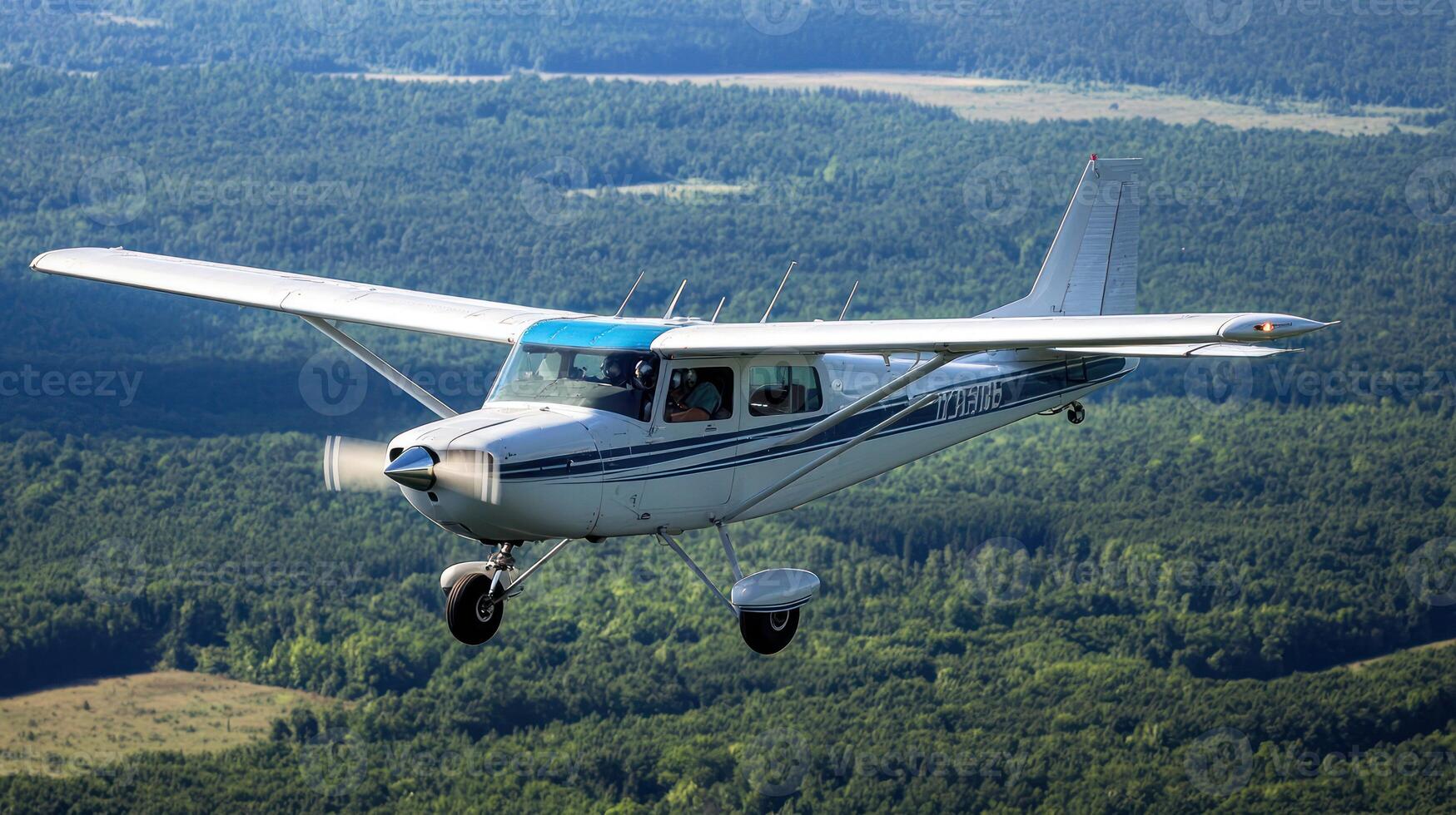 A small white airplane flying over a forested landscape with a clear blue sky. photo