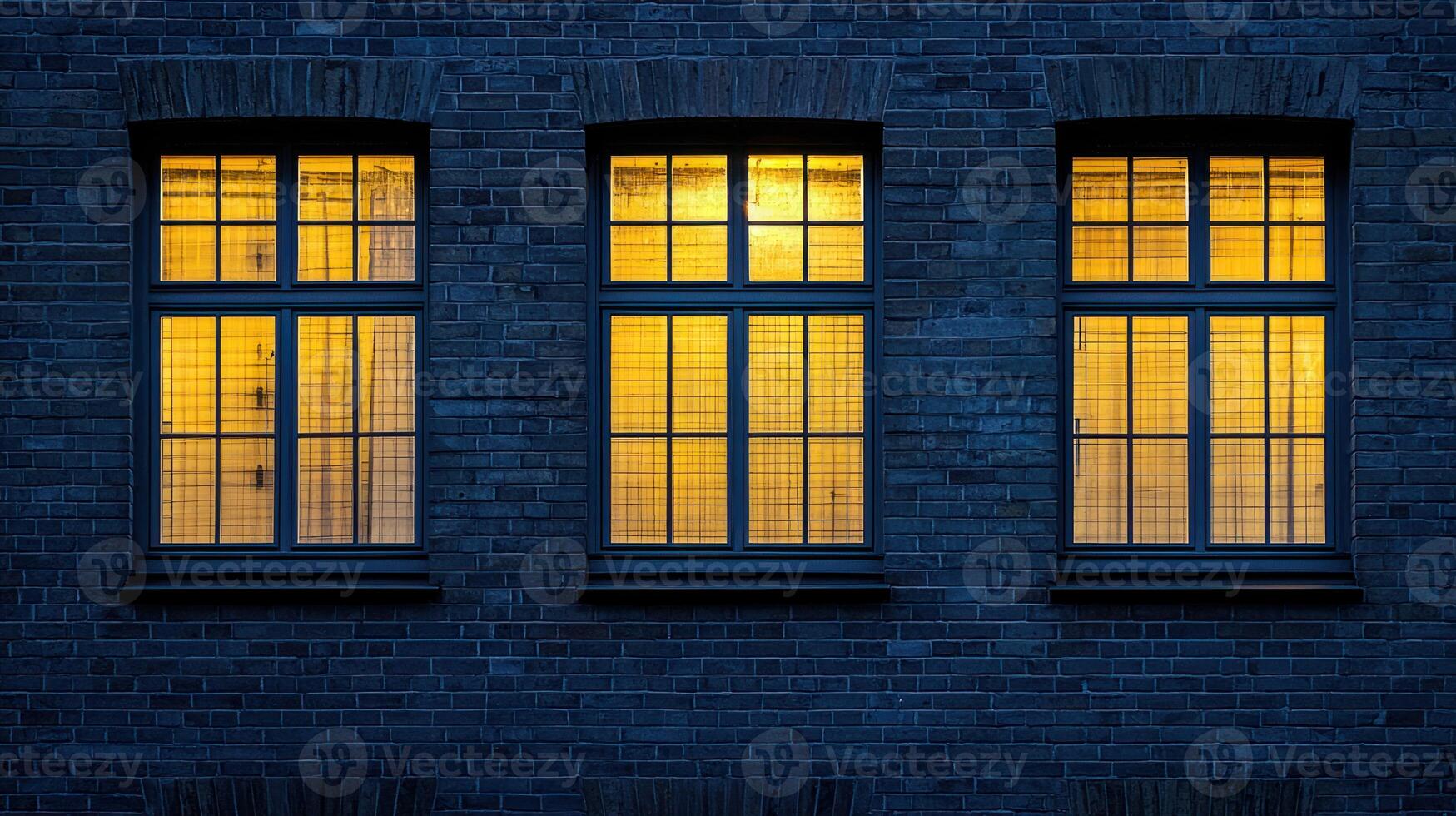 Three windows with yellow lights on, set against a dark brick wall photo