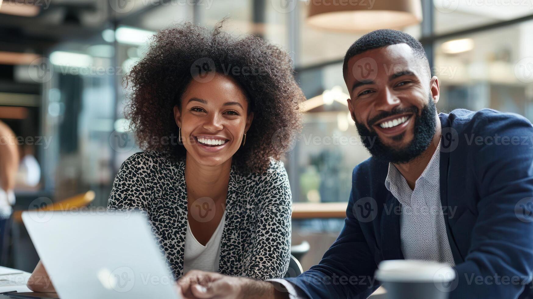 A smiling man and woman sitting at a table with a laptop, in a modern office setting. photo