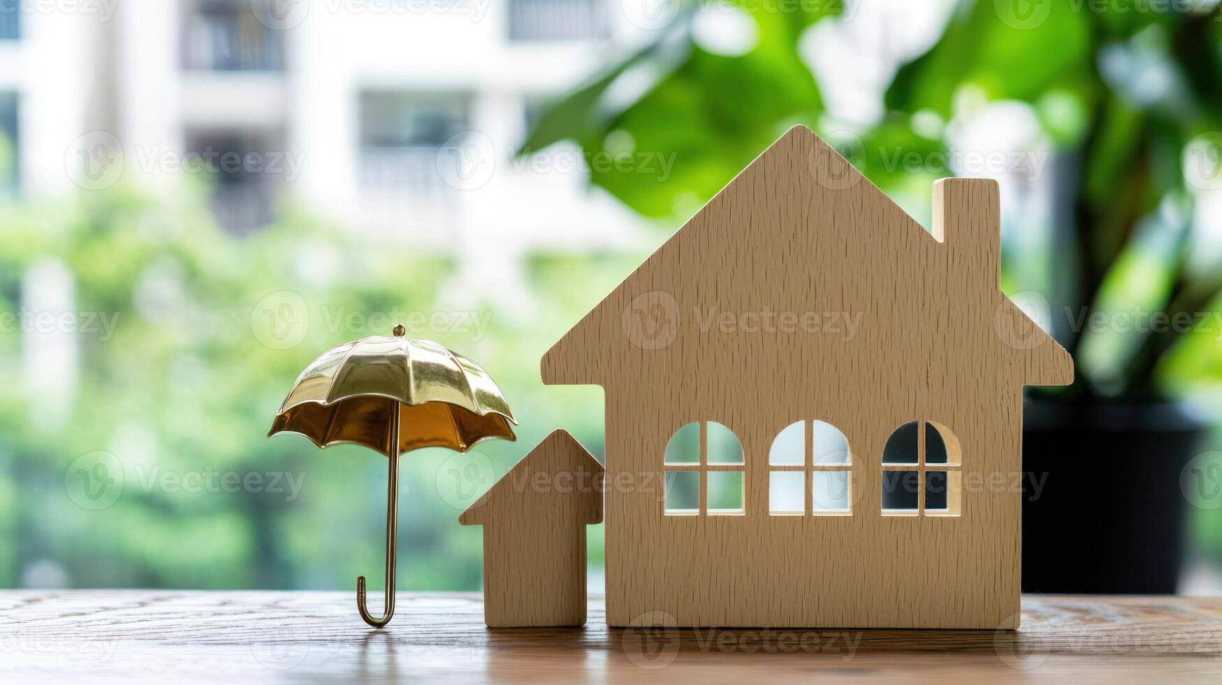 A wooden house model with a golden umbrella on a wooden table in front of a green plant and a blurred building in the background. photo