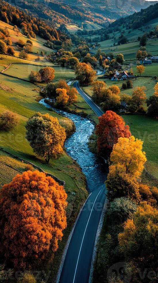 Golden autumn foliage along winding road beside tranquil river in scenic valley landscape photo