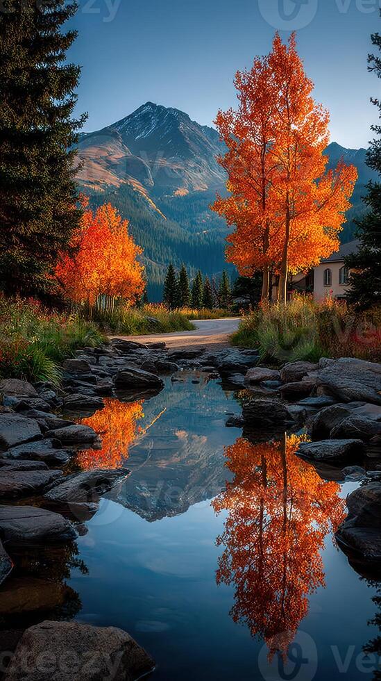 Vibrant autumn colors reflect in calm water near a mountain landscape under a clear blue sky photo