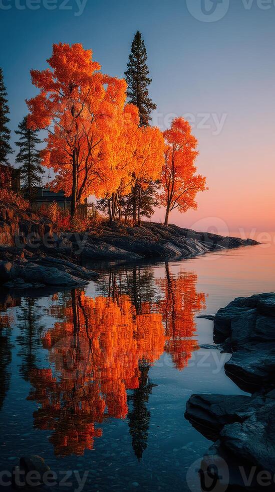 Autumn trees reflecting on calm water at sunset in a serene lakeside landscape photo