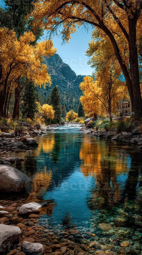 Autumn landscape with vibrant yellow trees and calm river reflecting the blue sky in a serene mountain setting photo