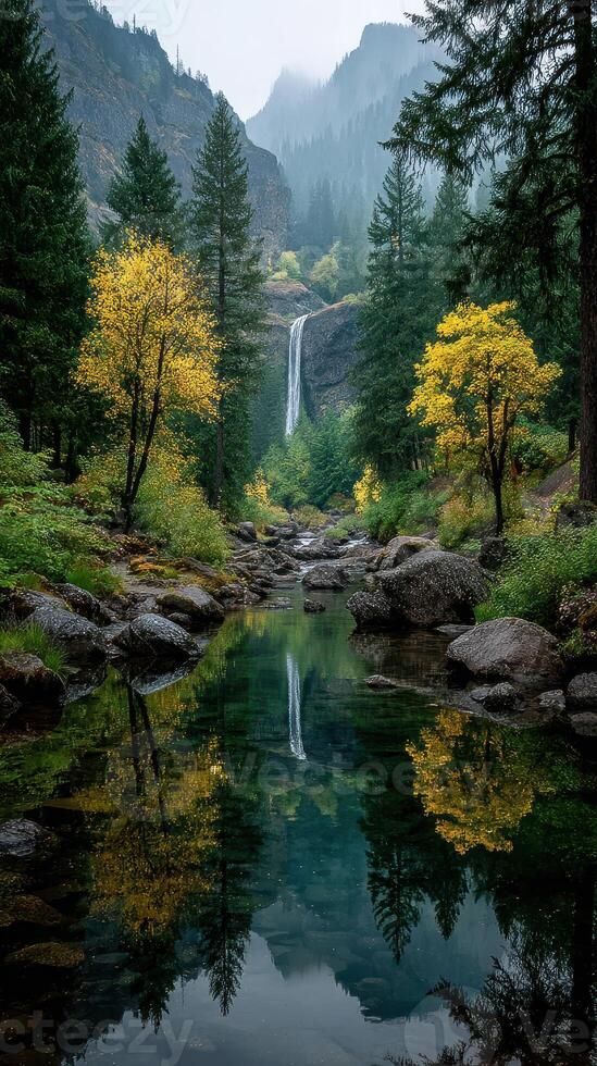 Waterfall cascades down rocky cliffs surrounded by autumn trees in misty mountain landscape photo