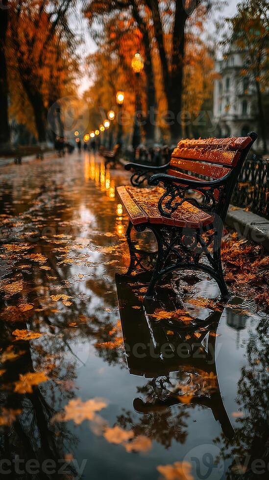 Rain creates a serene atmosphere around a park bench surrounded by autumn leaves in a golden-hued urban landscape photo