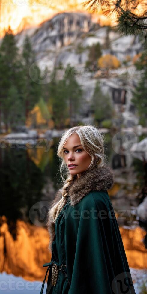 A beautiful blonde woman in a green cloak standing in front of a mountain photo