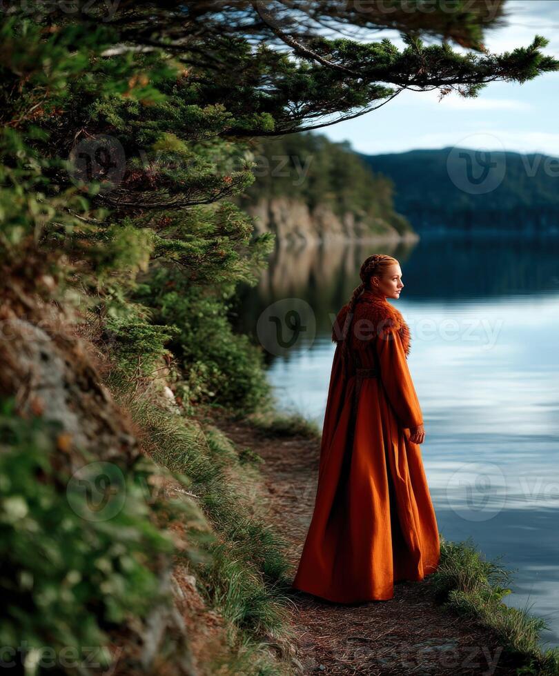 Viking woman in orange cloak standing by tranquil lake at sunset photo