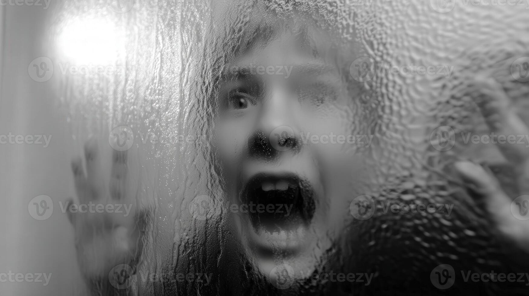 Child expressing fear behind frosted glass during evening hours photo