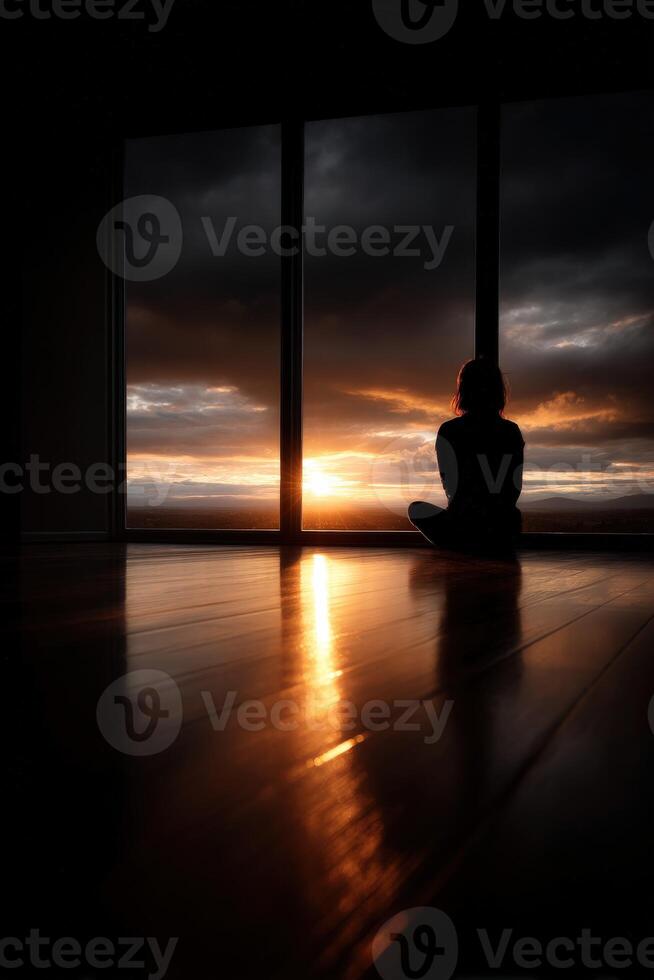 Silhouetted figure watches sunset through large windows in a serene setting photo