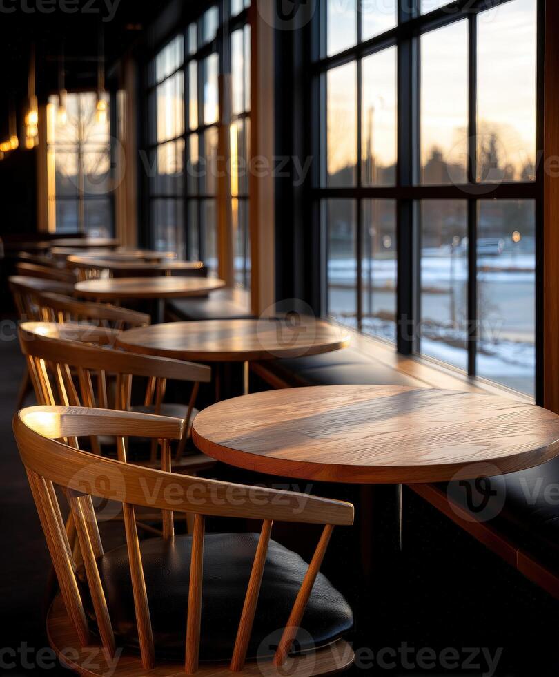 Elegant wooden tables and chairs by large windows during sunset hours photo