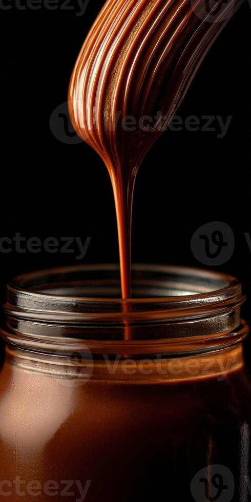 Chocolate sauce drizzled from a whisk into a glass jar at a kitchen photo