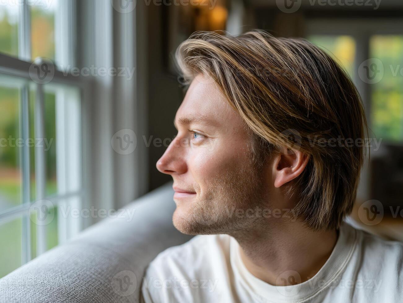 Man gazing thoughtfully out of a window in a cozy home setting photo