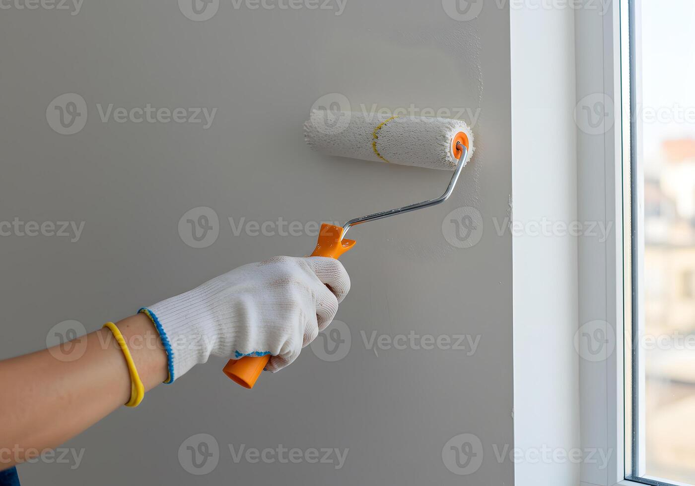 A person in white gloves is painting a wall with a roller photo