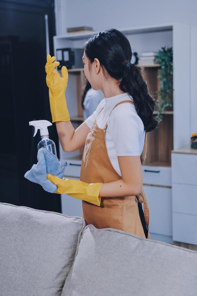A woman in an apron and rubber gloves cleaning a couch photo