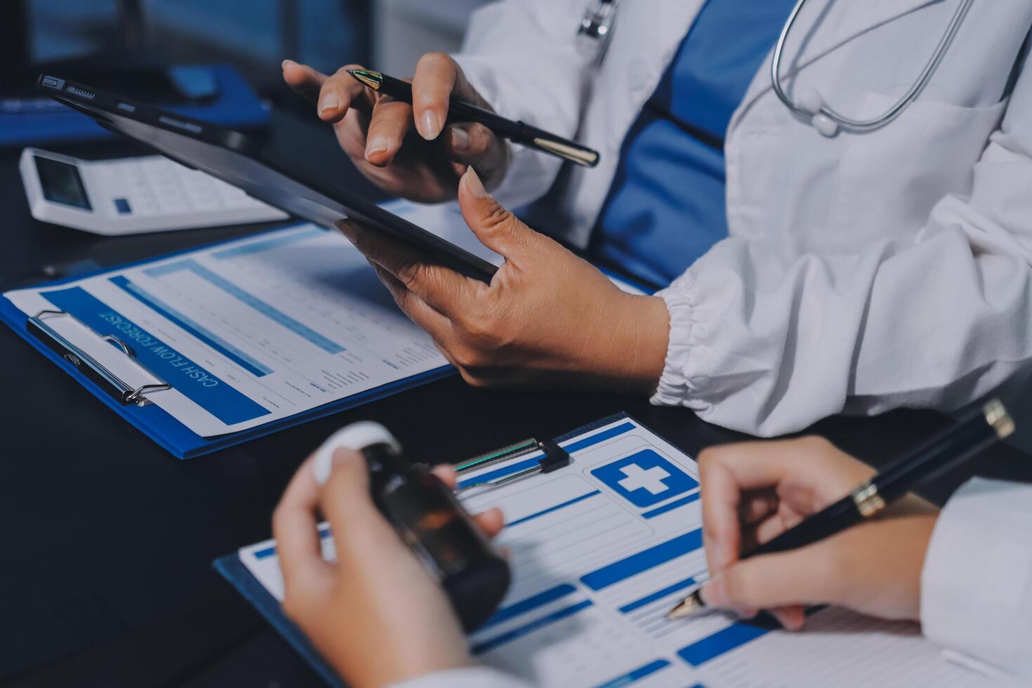 A doctor is using a tablet while two other people look on photo