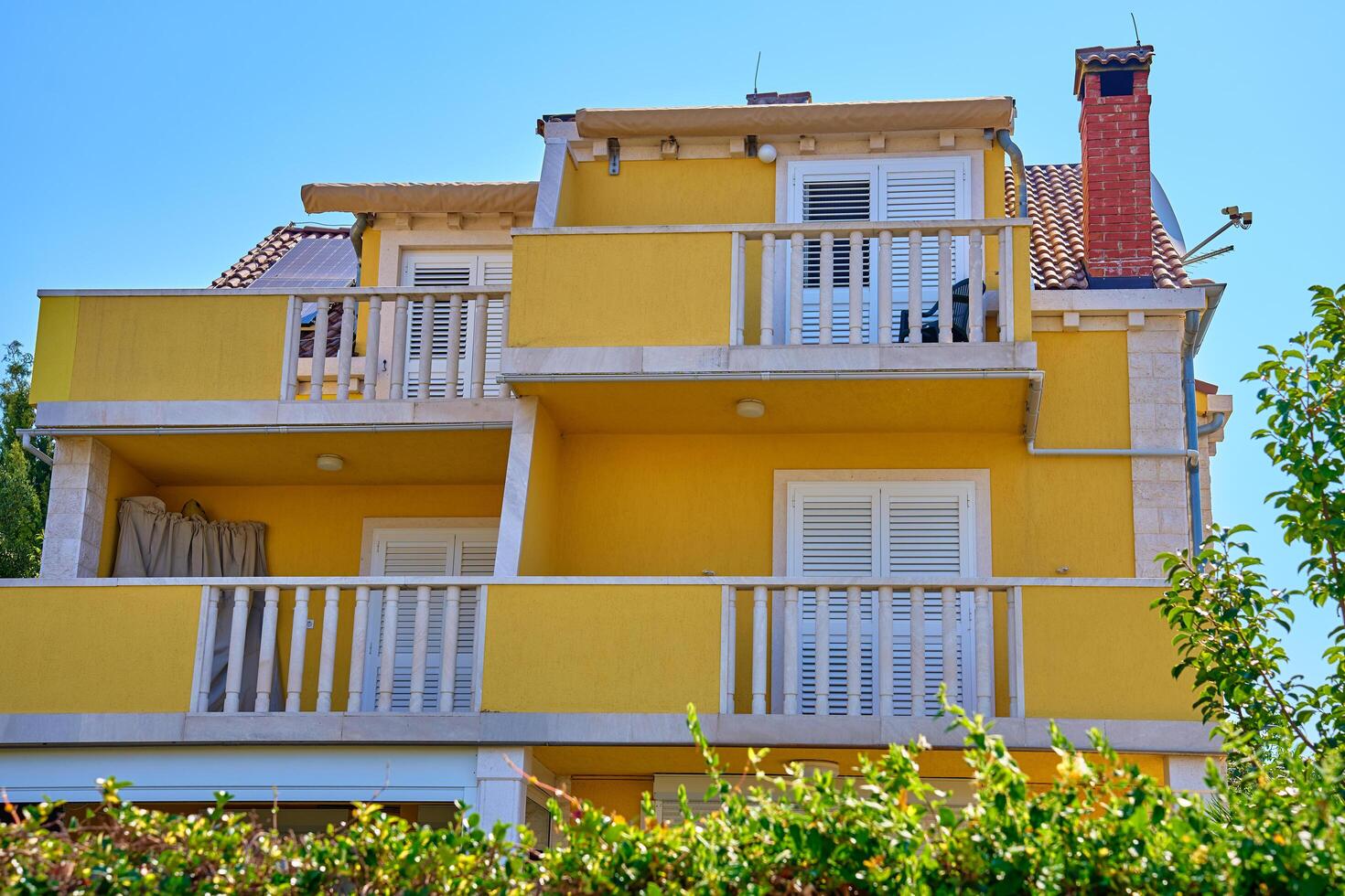 Rogoznica, Croatia, 2024 - Vibrant yellow villa with white shutters, balcony and lush greenery. Traditional architecture in Croatian village photo