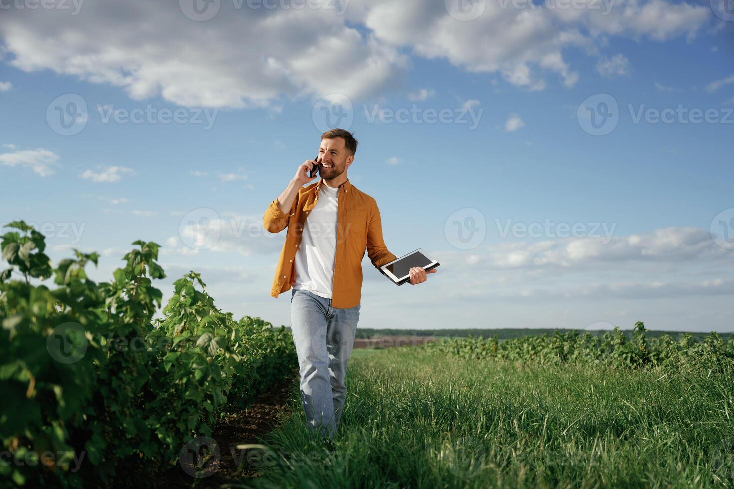 Talking by, phone, holding notepad. Handsome man is on the agricultural field at daytime photo