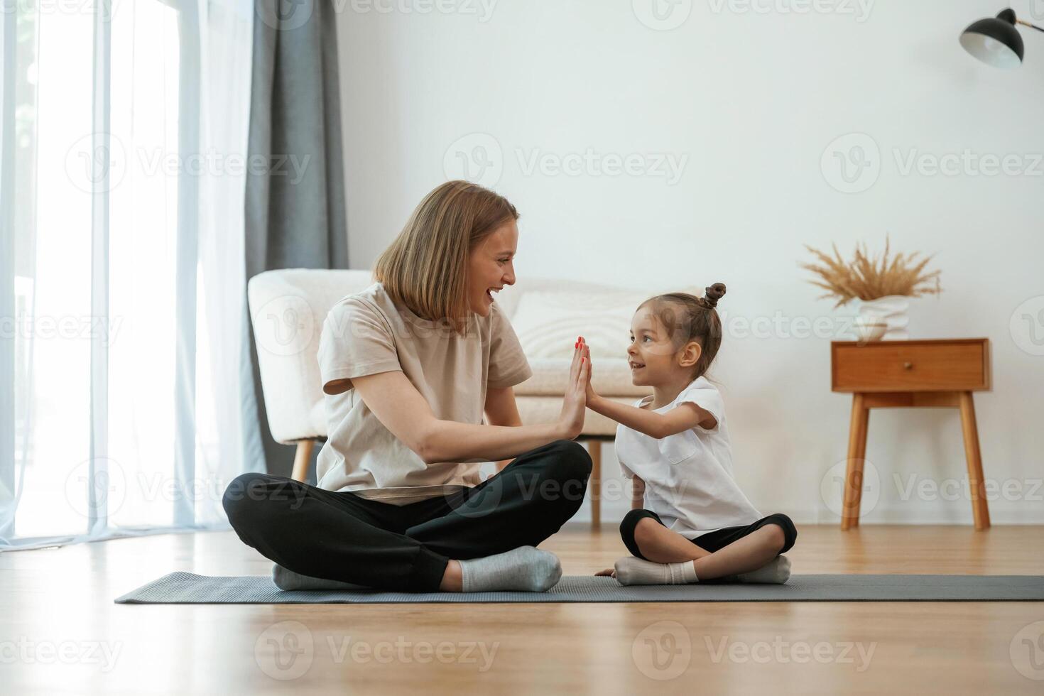 Well done, doing high five. Young woman with little girl are doing yoga at home photo