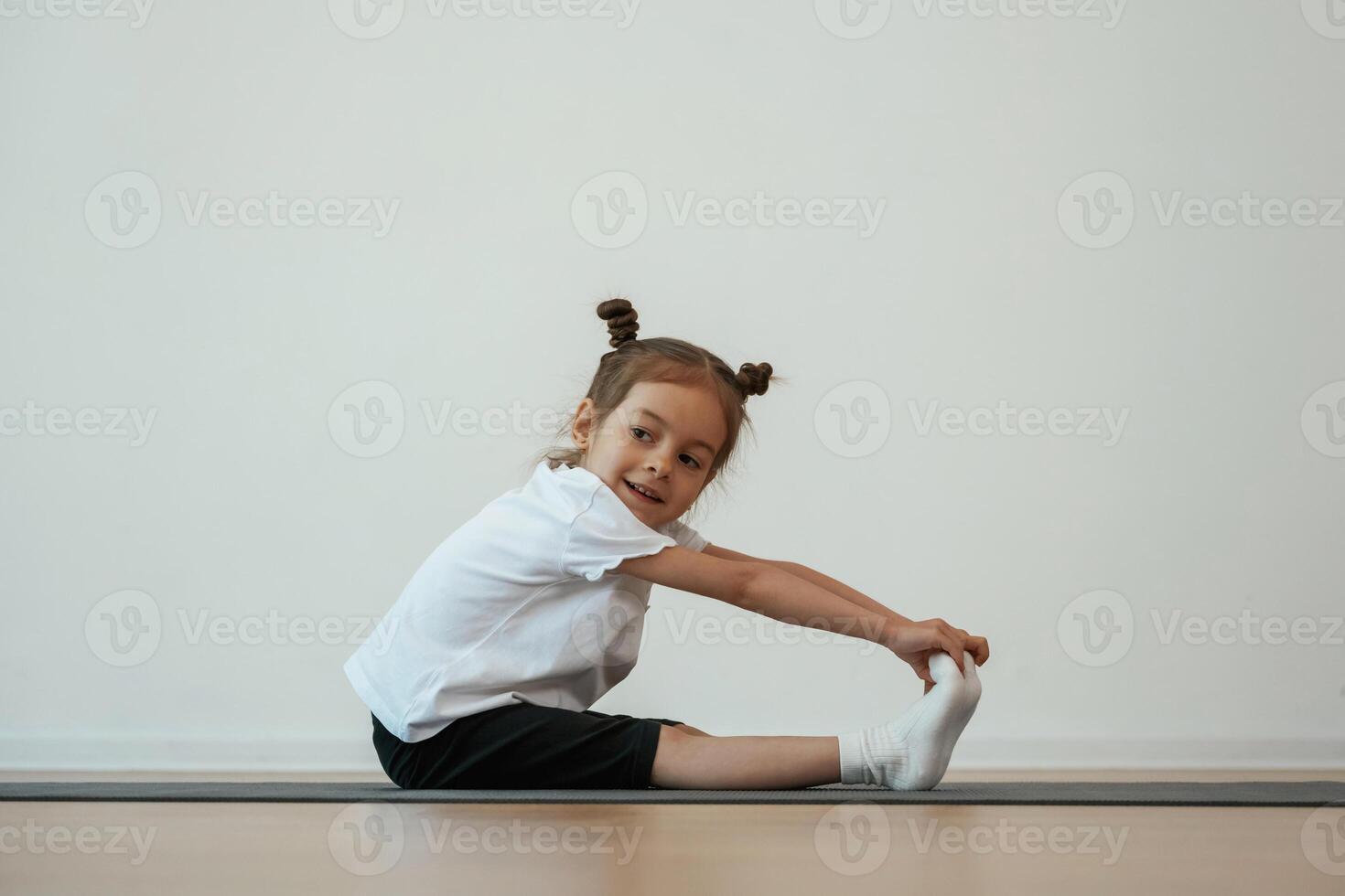Side view, stretching. Cute little girl is sitting on the yoga mat and doing exercises photo