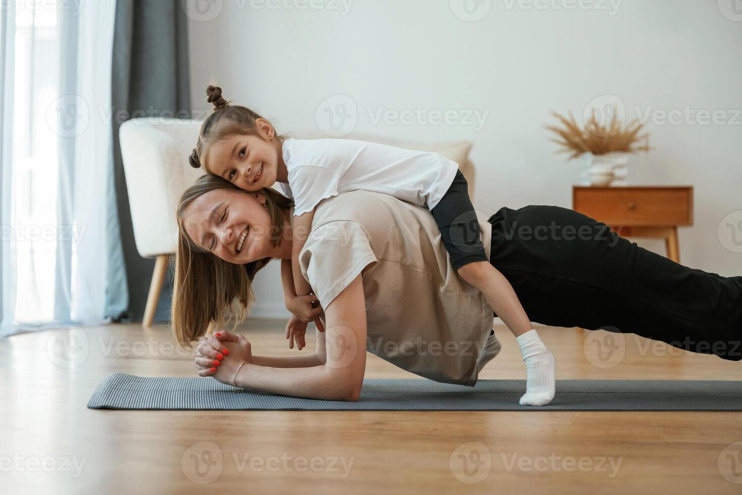 Lying ,down on the back of mother. Young woman with little girl are doing yoga at home photo