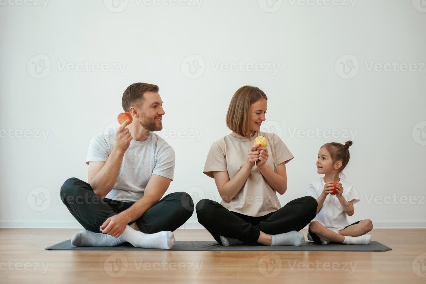 With apples in hands. Family ,of ,mother, father and daughter are doing yoga at home photo