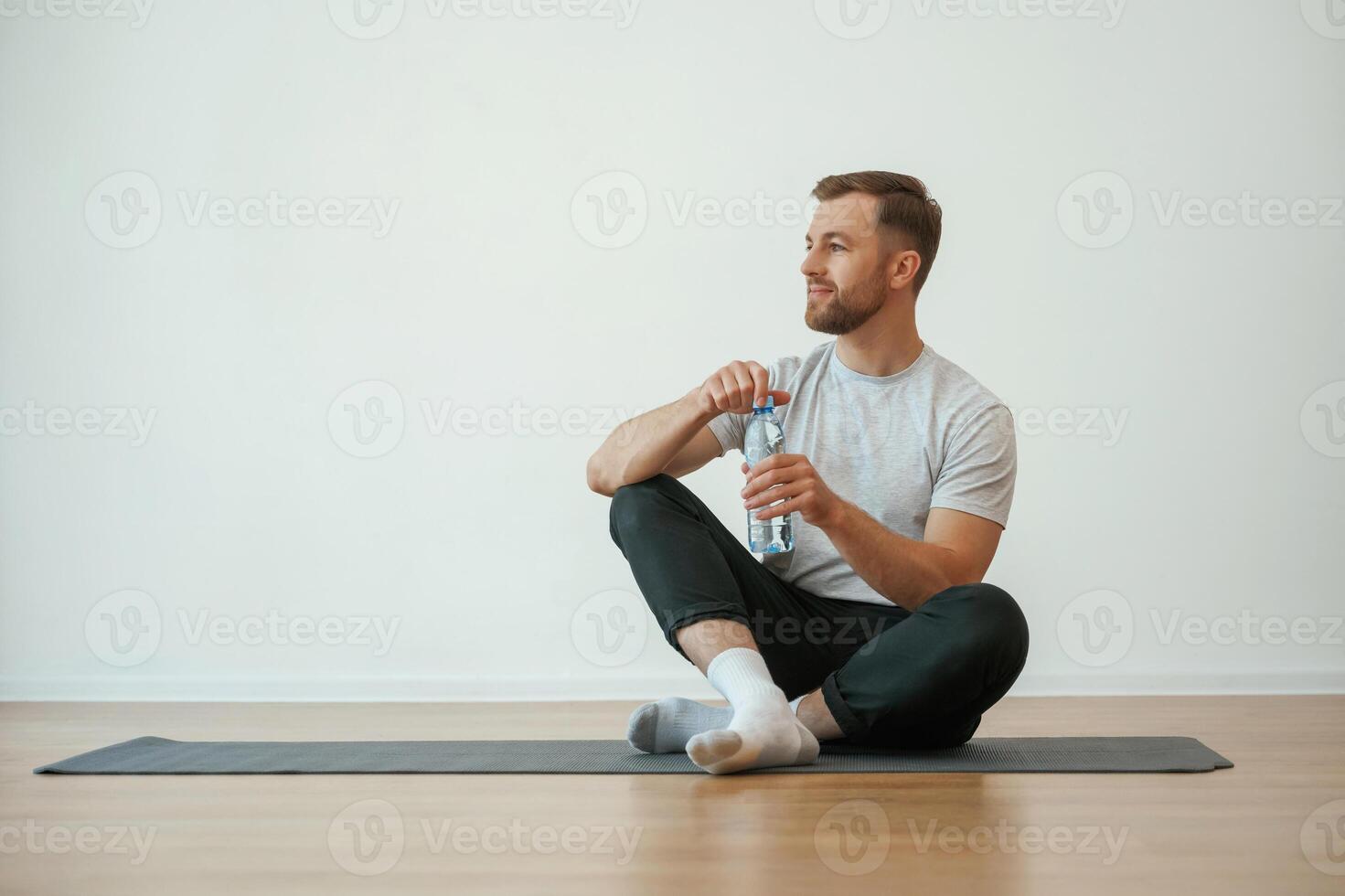 Taking ,a break, with bottle of water. Yoga man is sitting on a mat at home photo