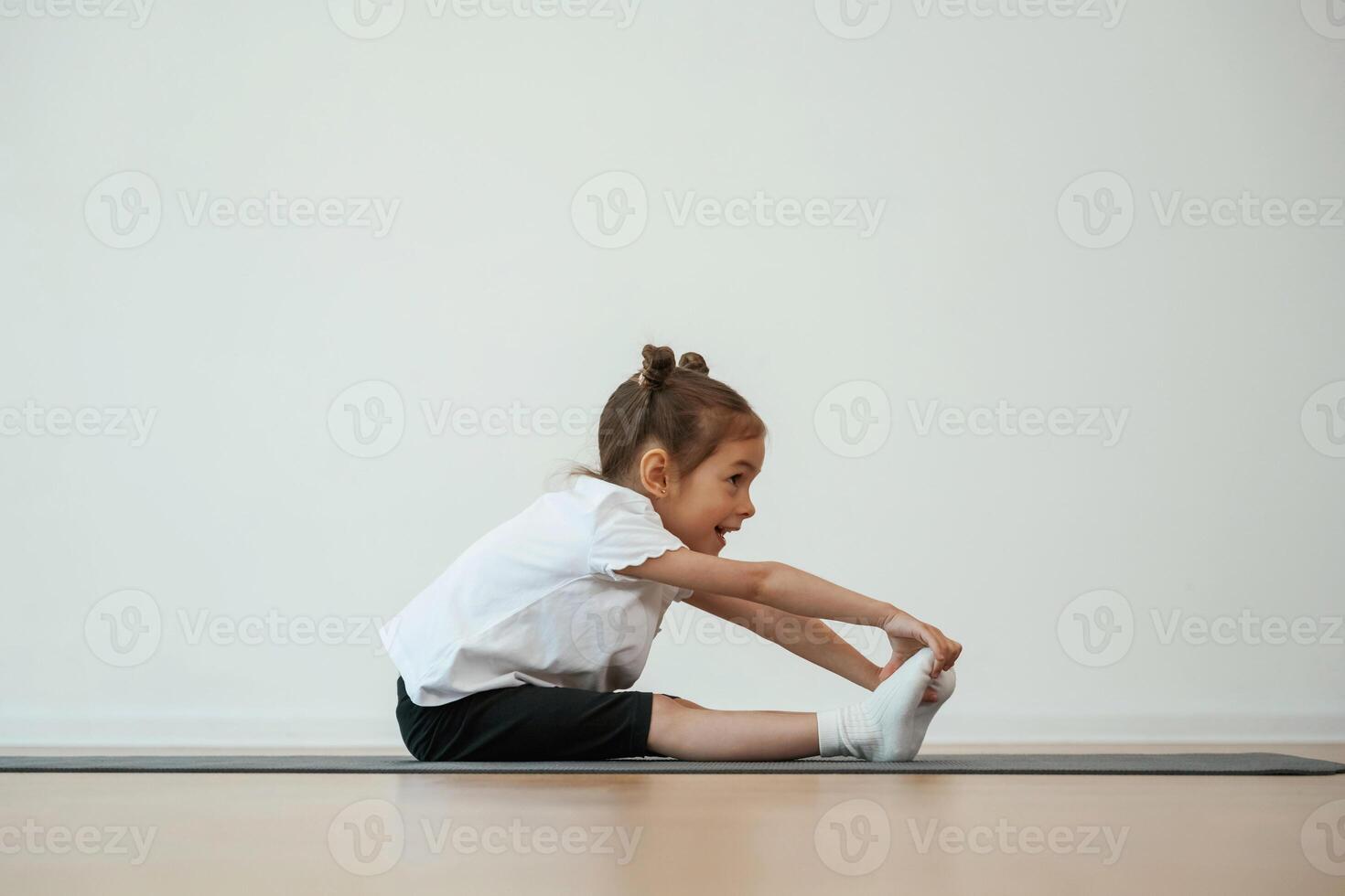 Side, view, stretching. Cute little girl is sitting on the yoga mat and doing exercises photo