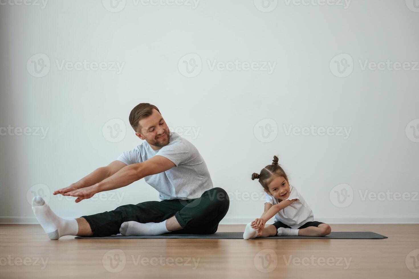 Teaching how to stretch ,the legs. Father with little daughter are doing yoga at home photo