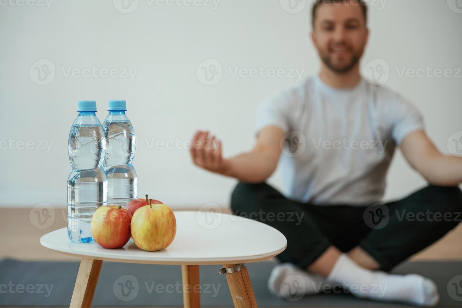Bottles of ,water and apples. Yoga man is sitting on a mat at home photo