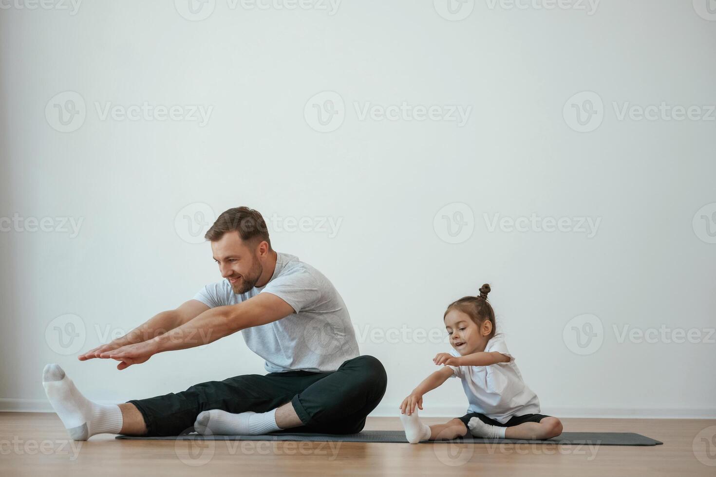 Teaching, how to stretch the legs. Father with little daughter are doing yoga at home photo