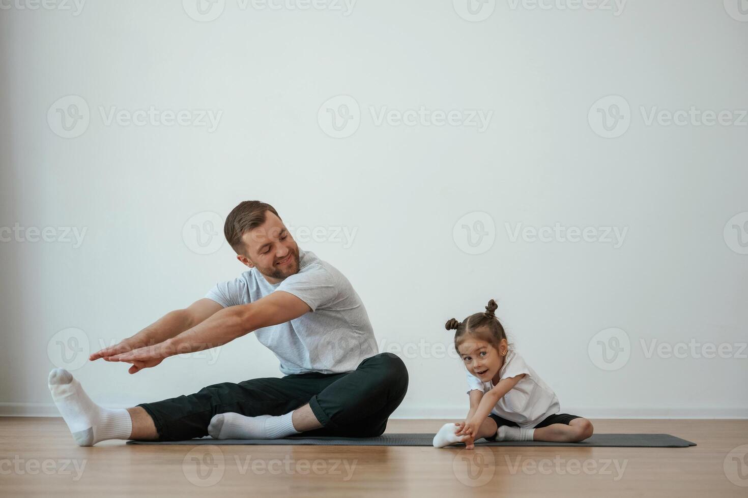 Teaching, how, to stretch the legs. Father with little daughter are doing yoga at home photo