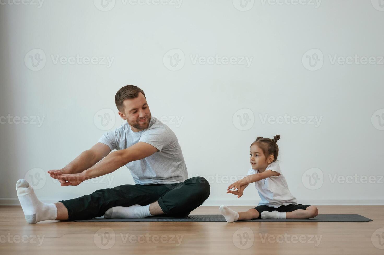 Teaching how, to stretch the legs. Father with little daughter are doing yoga at home photo