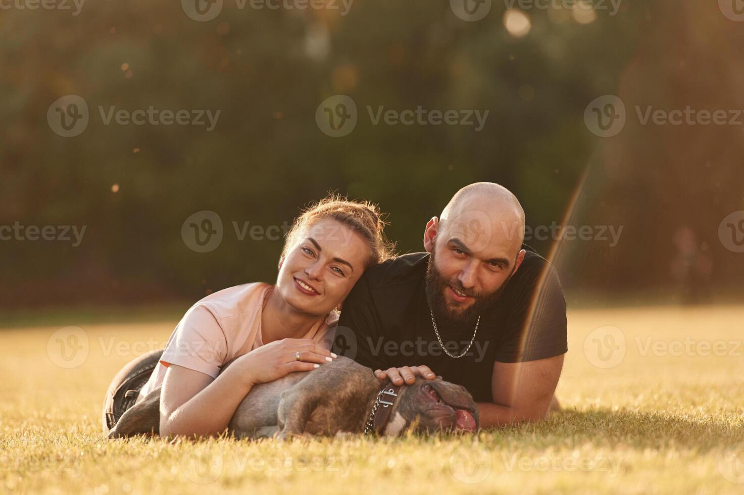 Calm, lying down on the ground. Man ,and, woman are with dog on the field photo