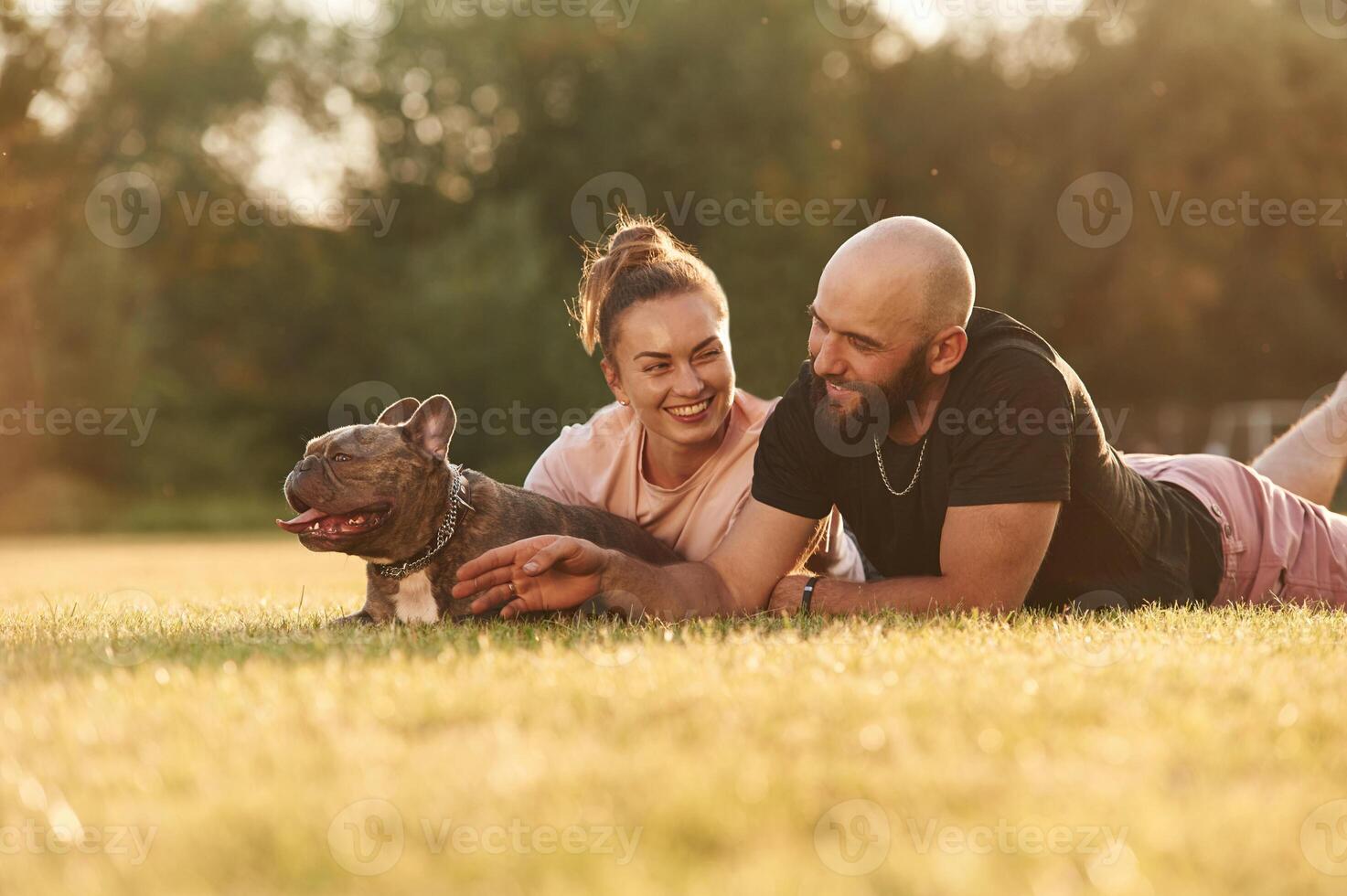 Calm, lying down on the ground., Man, and woman are with dog on the field photo