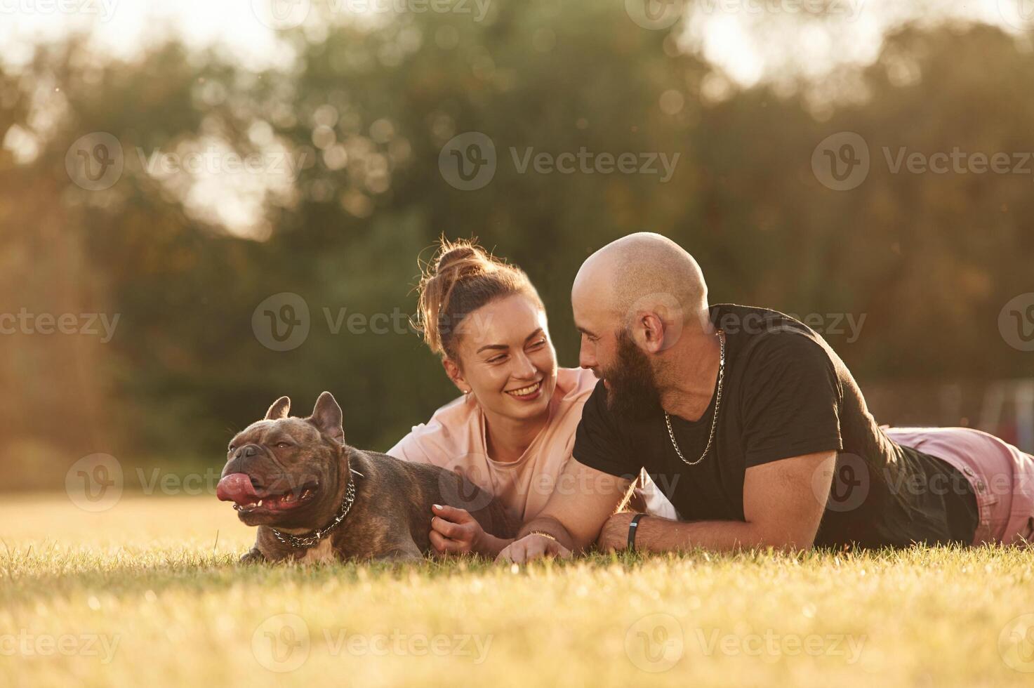 Calm, ,lying ,,down on the ground. Man and woman are with dog on the field photo