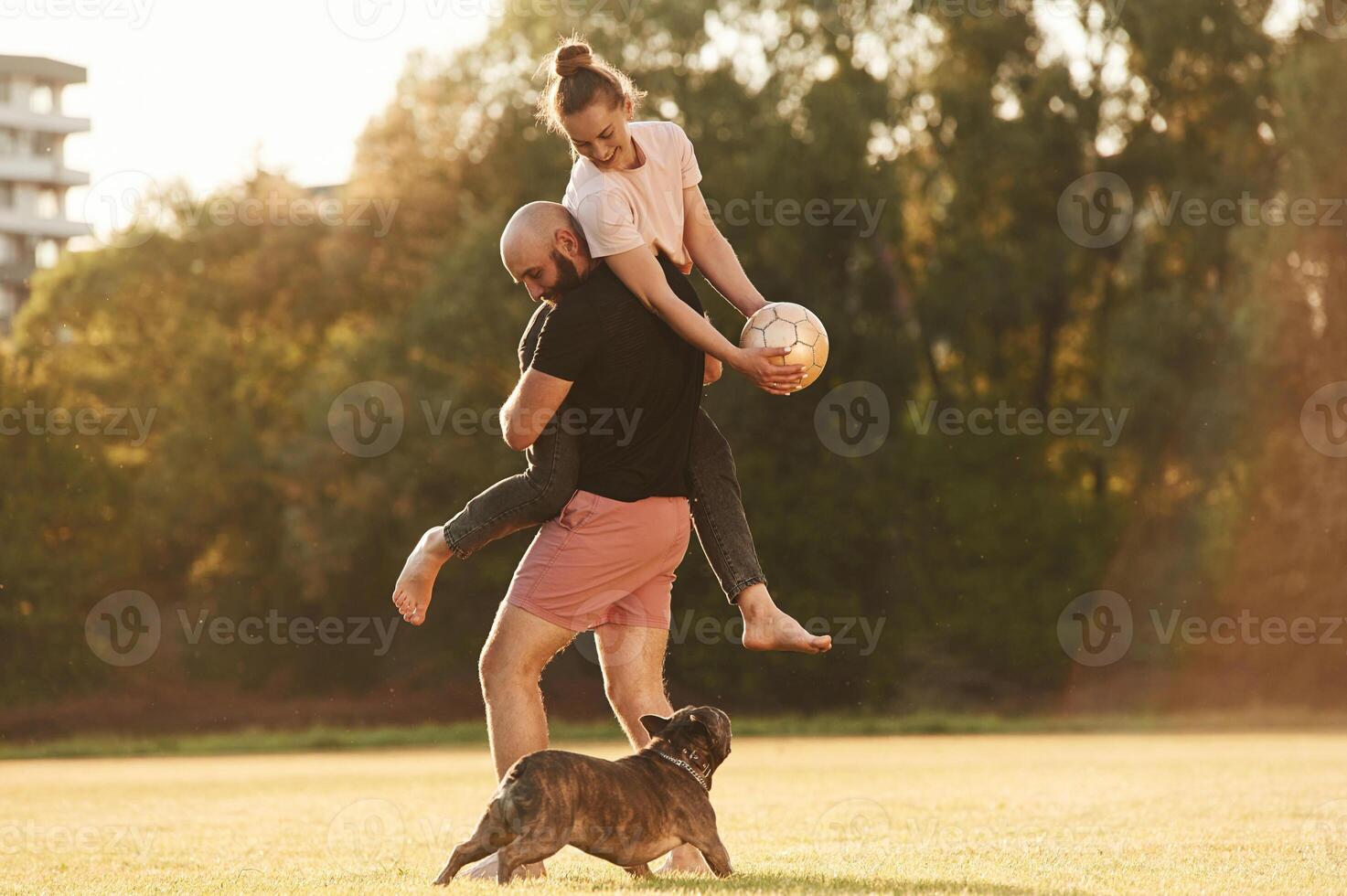 Using soccer ball, playing.. Man and woman are with dog on the field photo