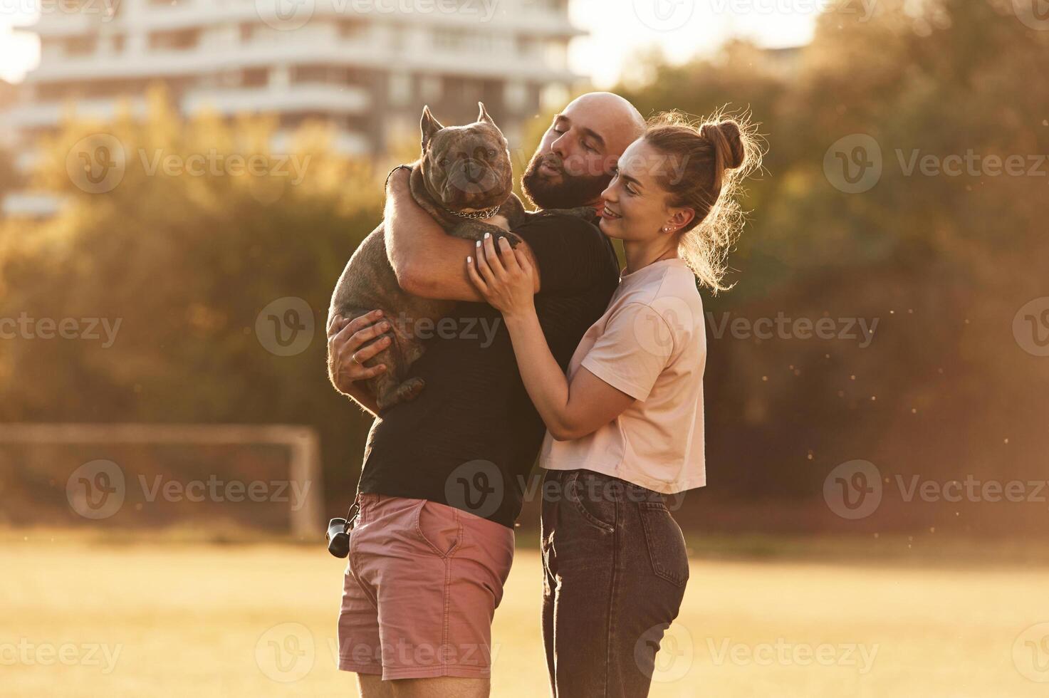 Side view, standing, and ,holding animal. Man and woman are with dog on the field photo