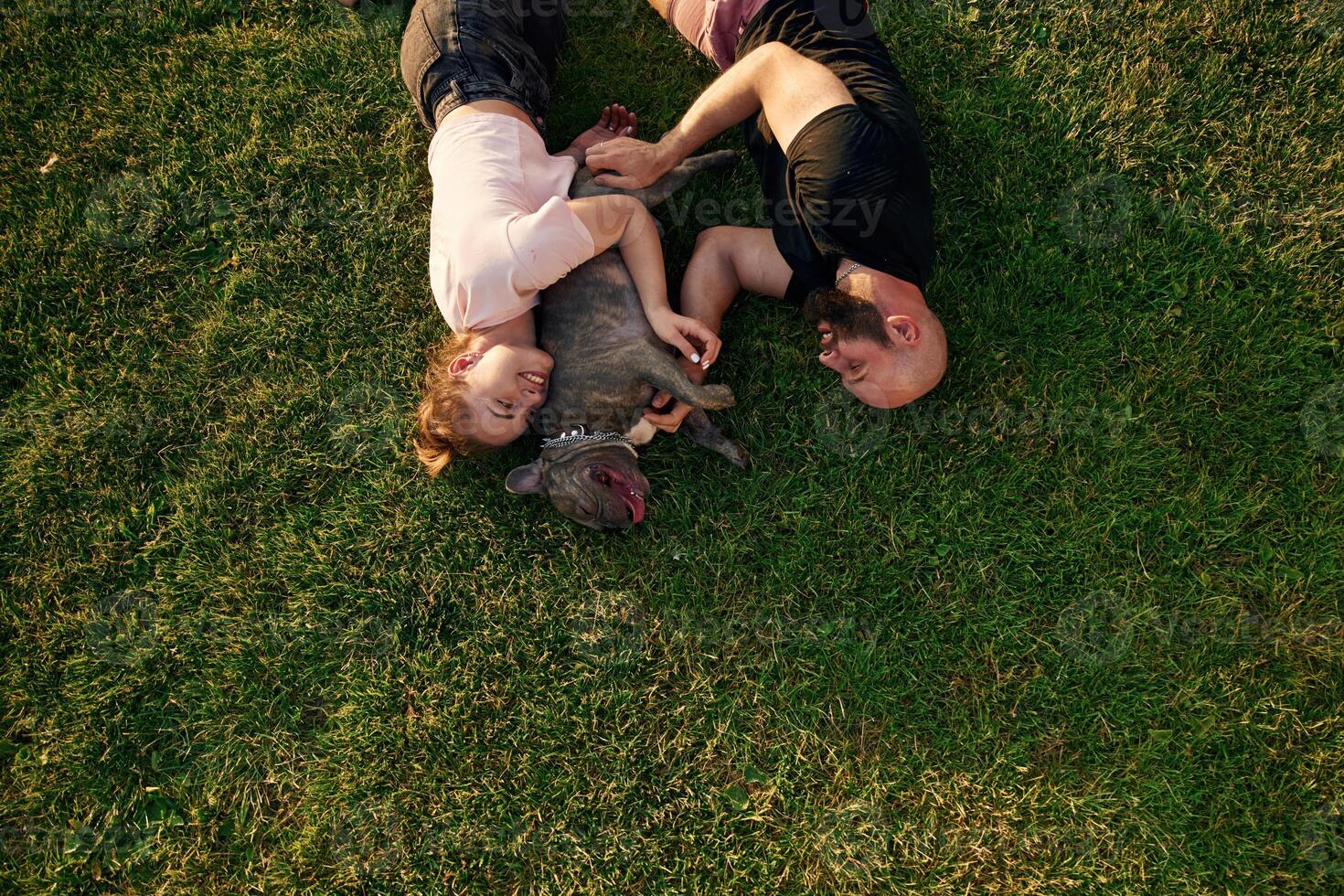 Top view, lying, on the grass. Man and woman are with dog on the field photo