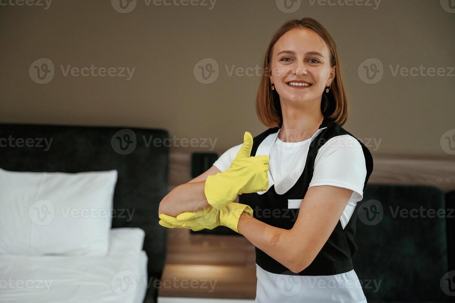 Thumb up ,gesture,, in yellow gloves. Young chambermaid is in hotel room photo