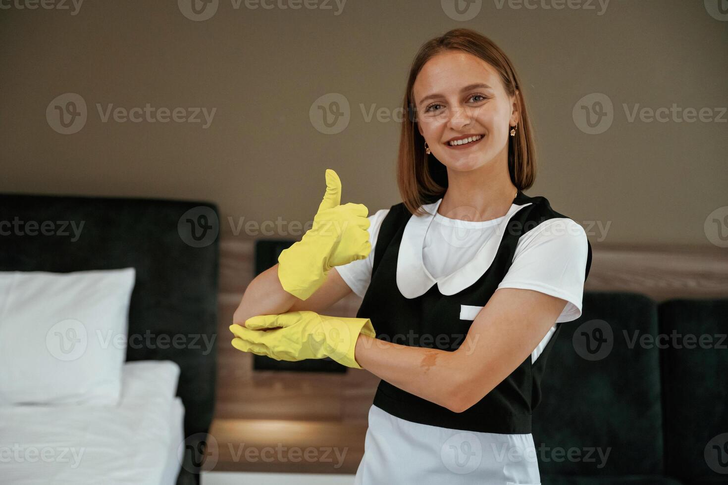 Thumb, up gesture, in yellow gloves. Young chambermaid is in hotel room photo