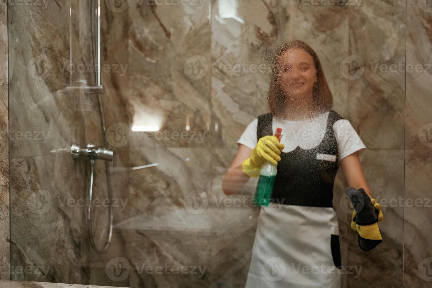 Green ,washing product, cleaning the glass in bathroom. Young chambermaid is in hotel room photo
